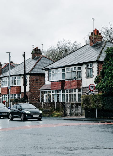 A row of older semi-detached houses with brick and rendered facades, featuring large bay windows and tiled pitched roofs, situated close to the street in a residential area. The houses have a mix of g